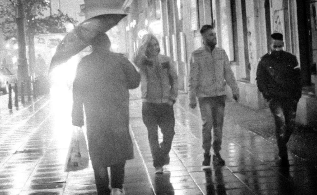 Umbrella-carrying pedestrian walking through bright rain mist beside other passersby